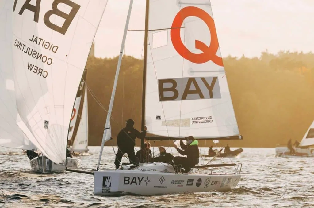 J/70s racing at golden hour with a red 'Q Bay' sponsor logo on the mainsail, Bundesliga Finals