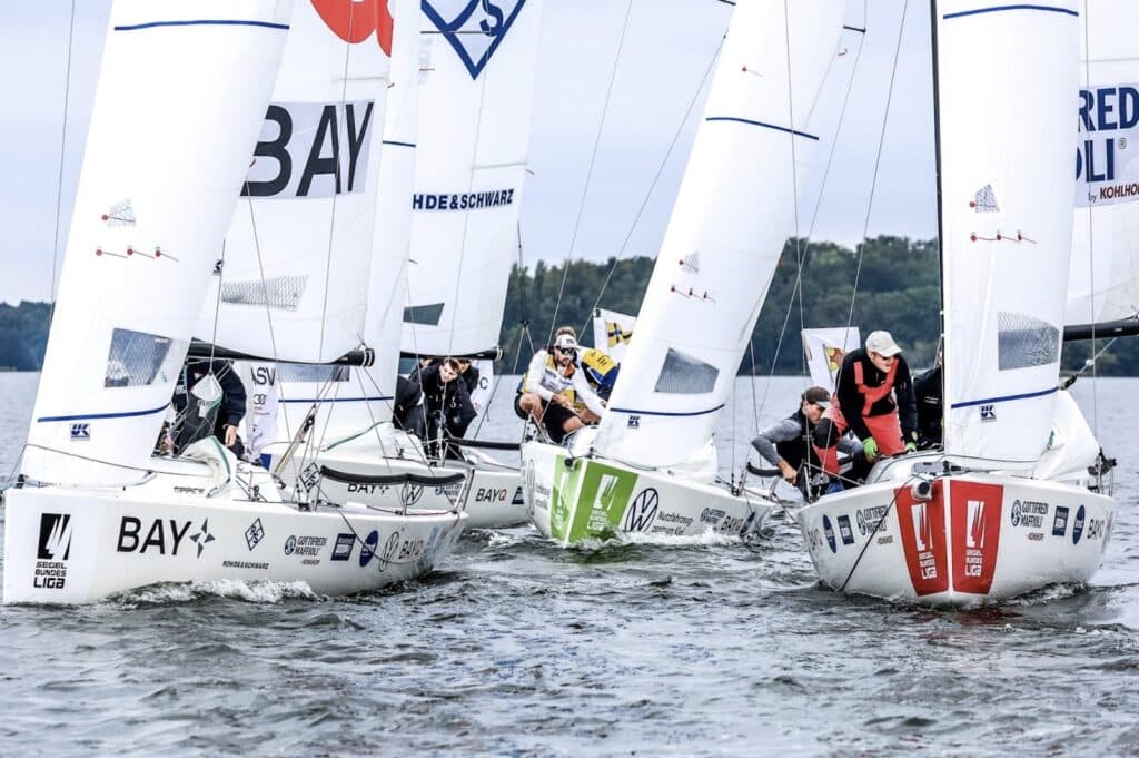 Four J/70 keelboats bunched together at a mark, sponsor logos visible on the sails