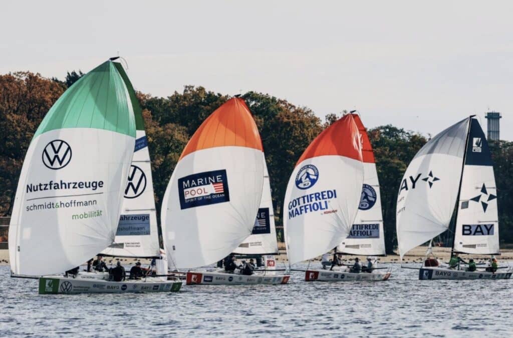 J/70 fleet reaching four abreast under green, orange and red sponsor spinnakers