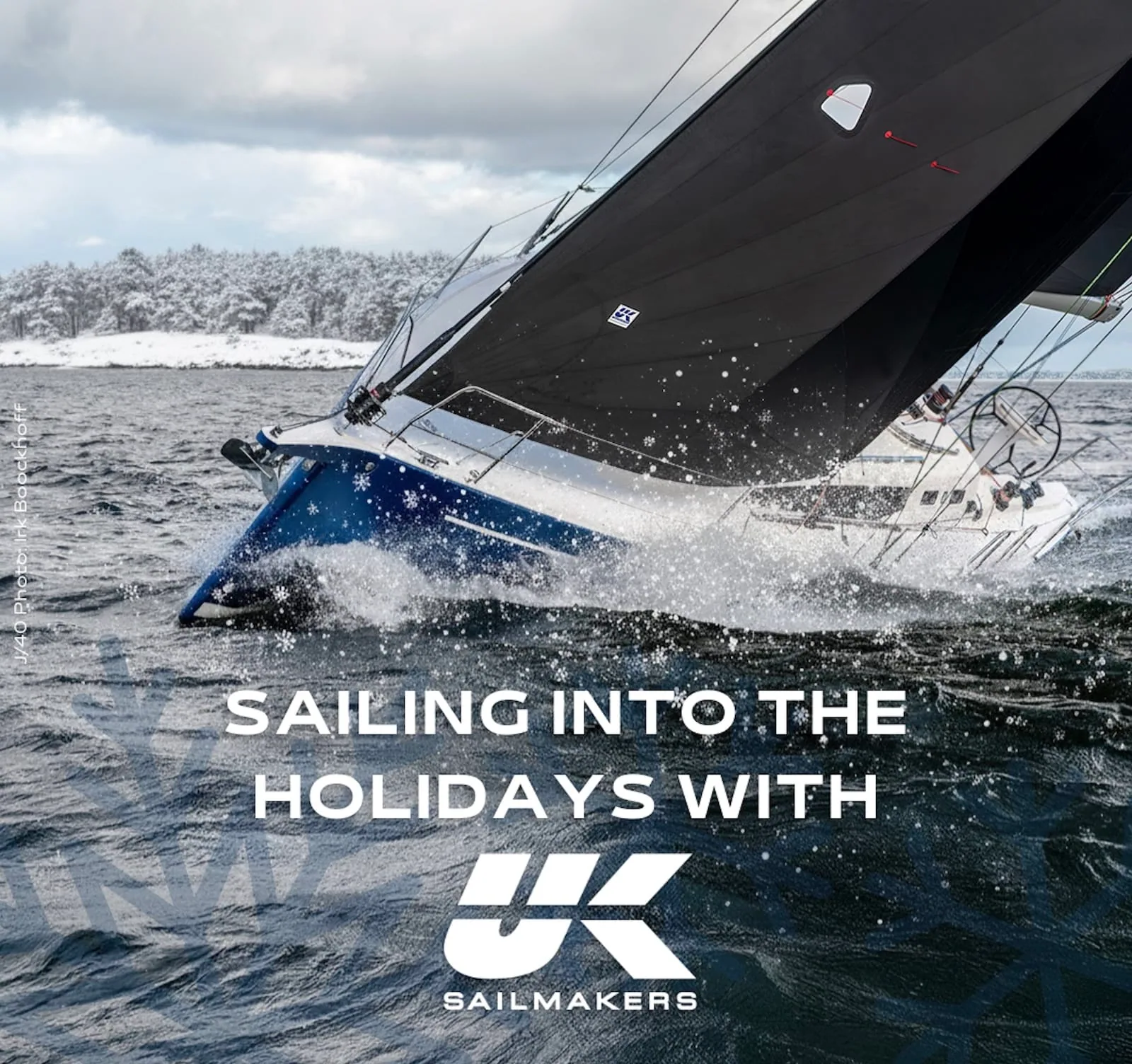 Yacht heeled hard through snow-dusted water with 'Sailing Into the Holidays' UK Sailmakers text