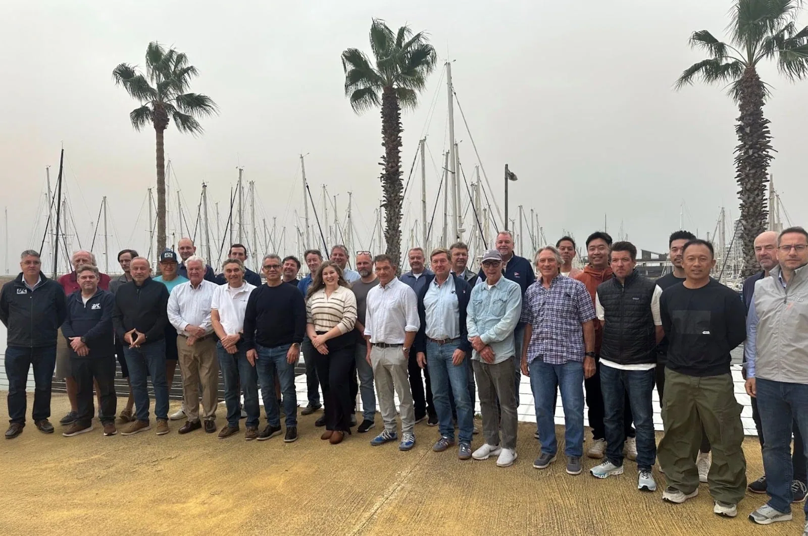Group photo of UK Sailmakers loft managers and staff gathered at a palm-lined marina