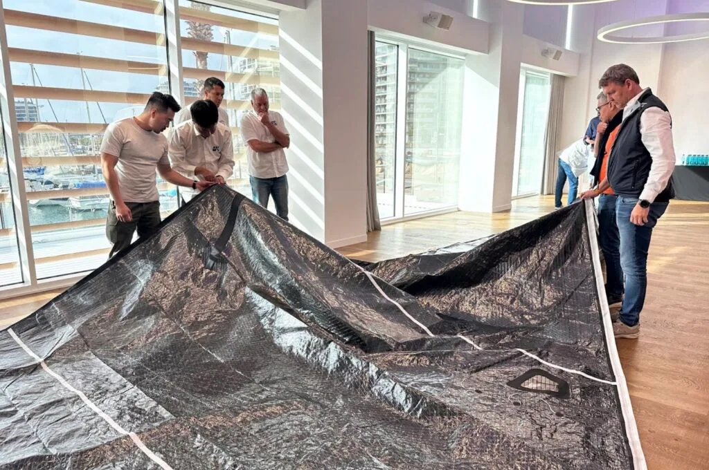 Team examining a black X-Drive® sail laid out flat on a meeting-room floor