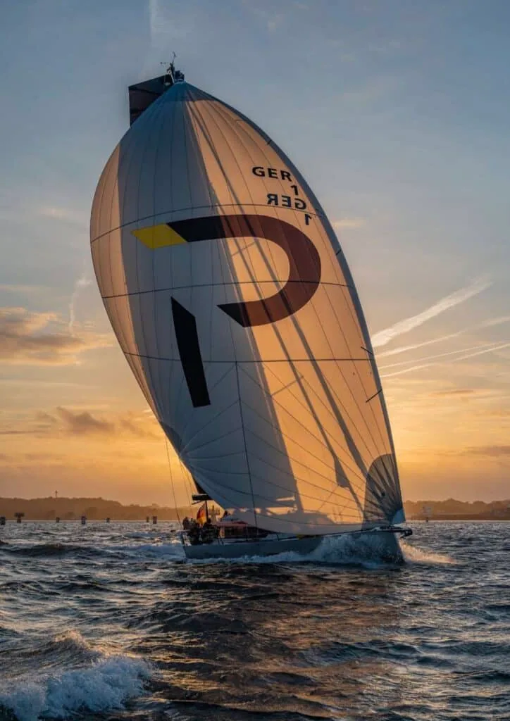 Pure 42 GER 1 flying a large asymmetric spinnaker with a bold 'P' logo at sunset