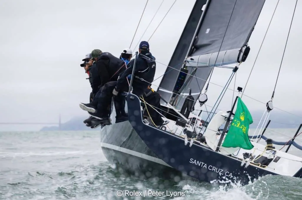 Farr 400 Astra bow crew hiking hard in choppy water, Bay Area shoreline behind