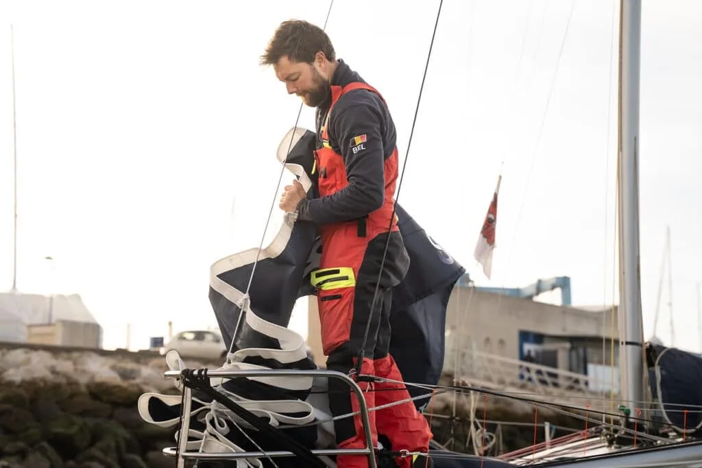 Solo offshore sailor in red foul-weather gear working the foredeck dockside