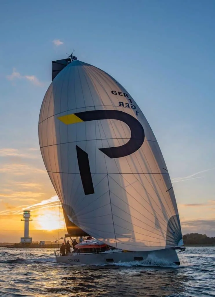 Pure 42 GER 1 flying her 'P' logo spinnaker past a lighthouse at sunset