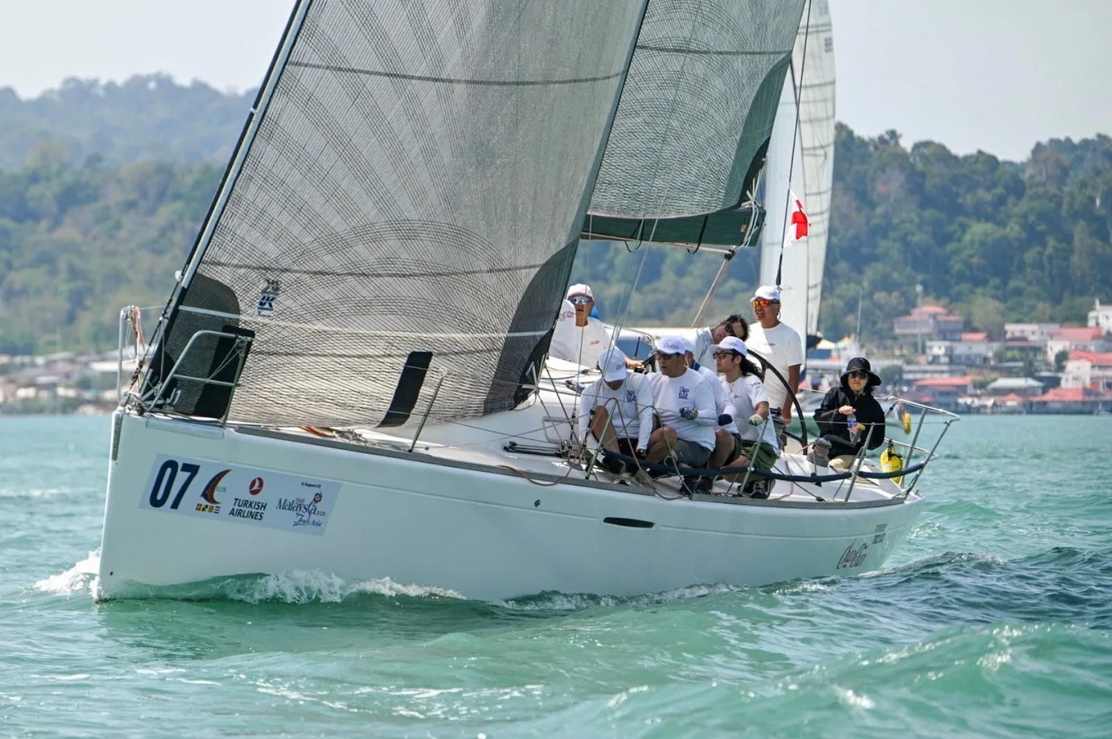 Sail number 07 racing close-hauled near a green shoreline at the Royal Langkawi Regatta