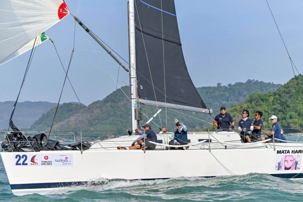 'Mata Hari', sail number 22, reaching under a dark mainsail off a tropical coast