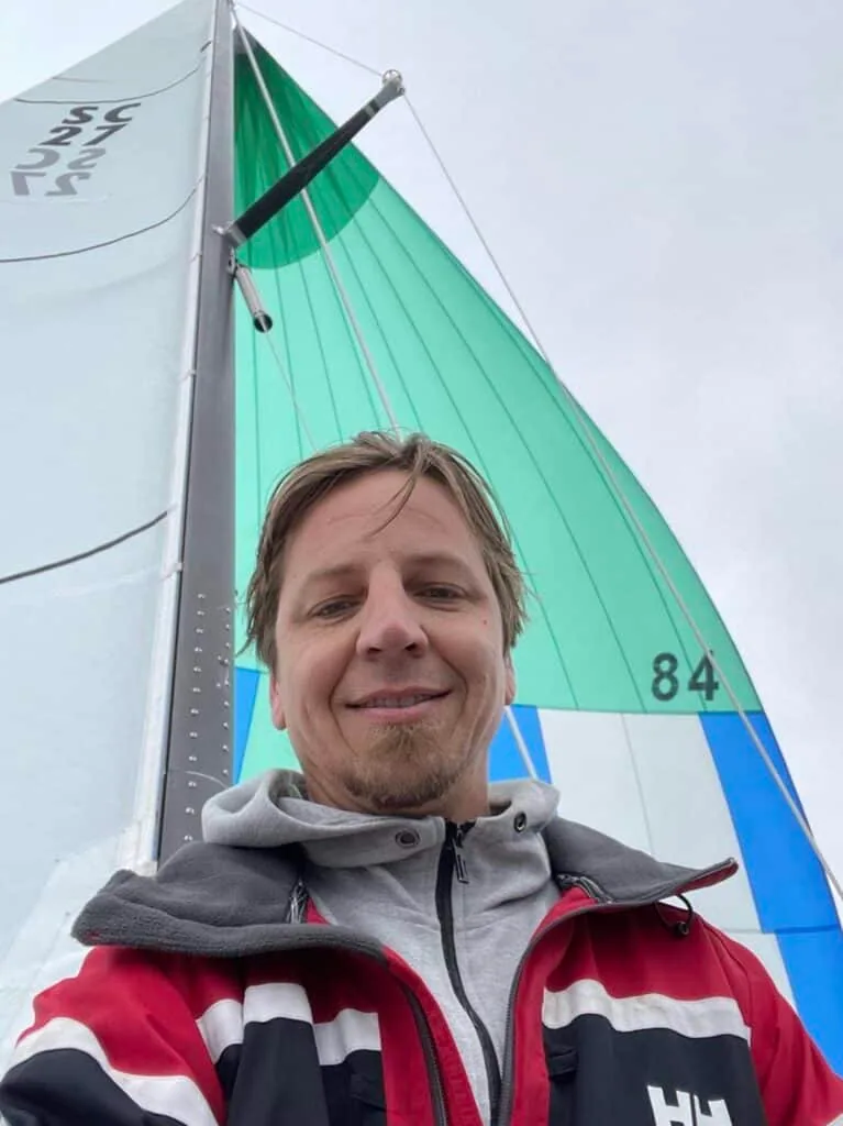 Kelly Sears smiling in a selfie in front of a green and blue racing mainsail