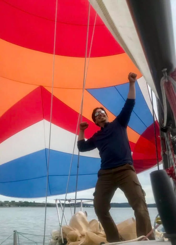 Sailor pumping both fists under a bright multicolor spinnaker on deck