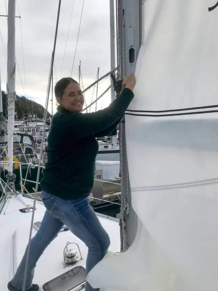 Steph Jarvis smiling while hoisting a sail at the mast, marina in the background