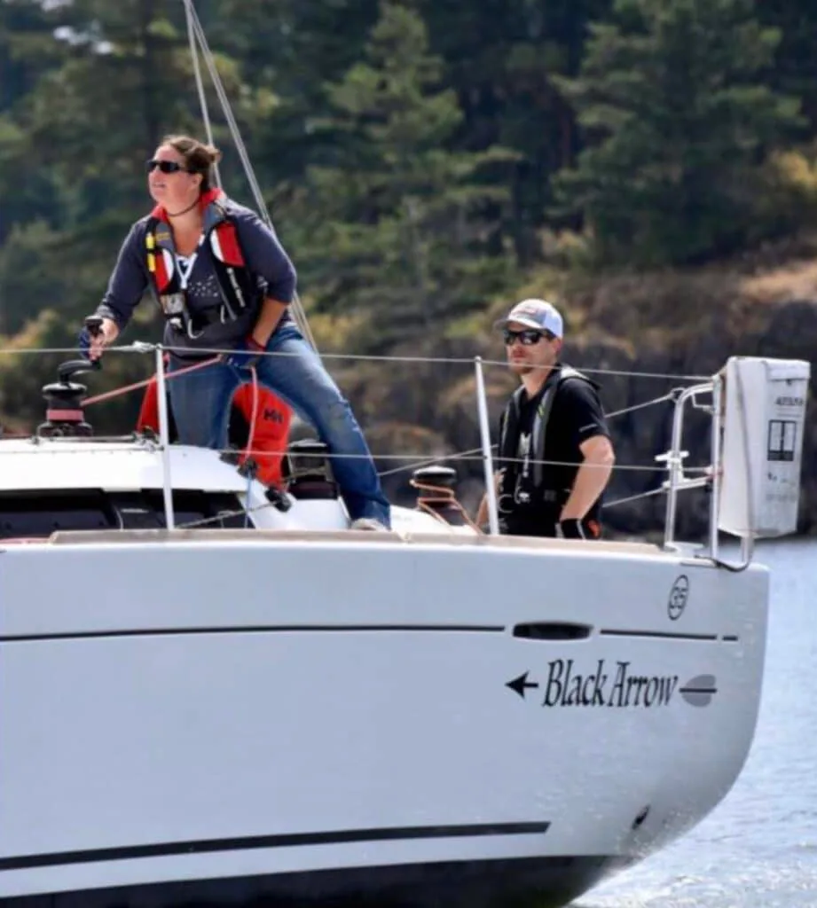 Crew trimming aboard 'Black Arrow' near a tree-lined shoreline