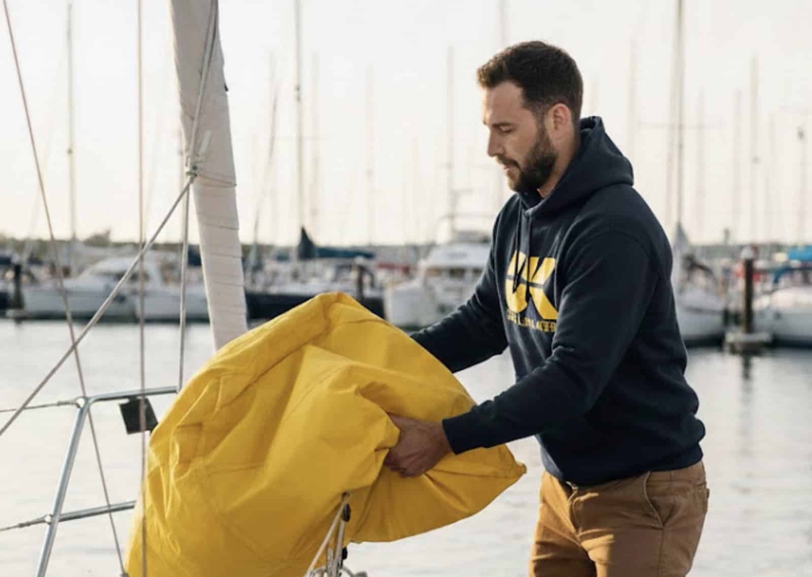 Man in UK Sailmakers hoodie folding a yellow sail bag on a dock