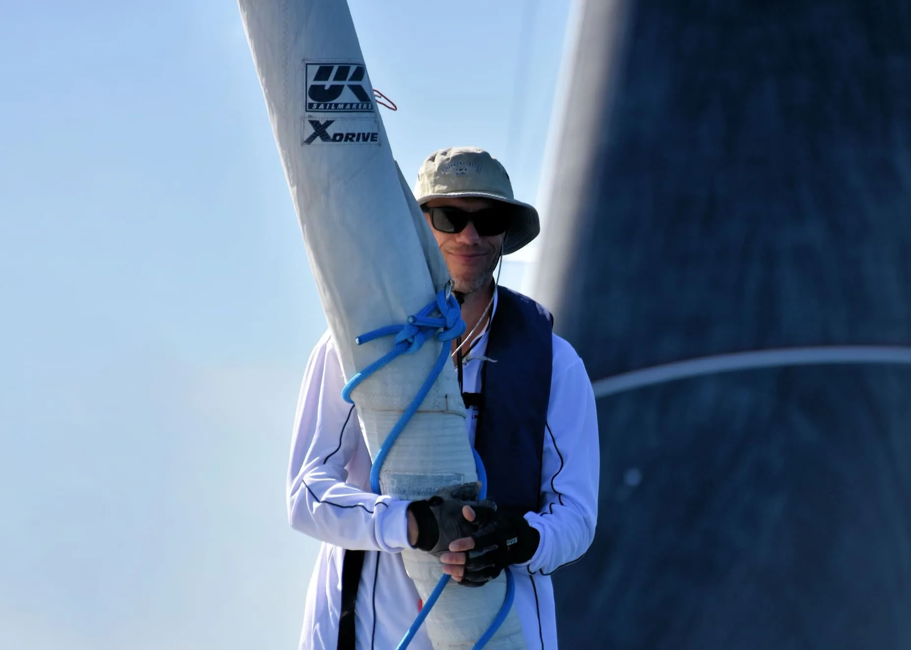 Sailor beside a rolled sail printed with the UK Sailmakers X-Drive® logo