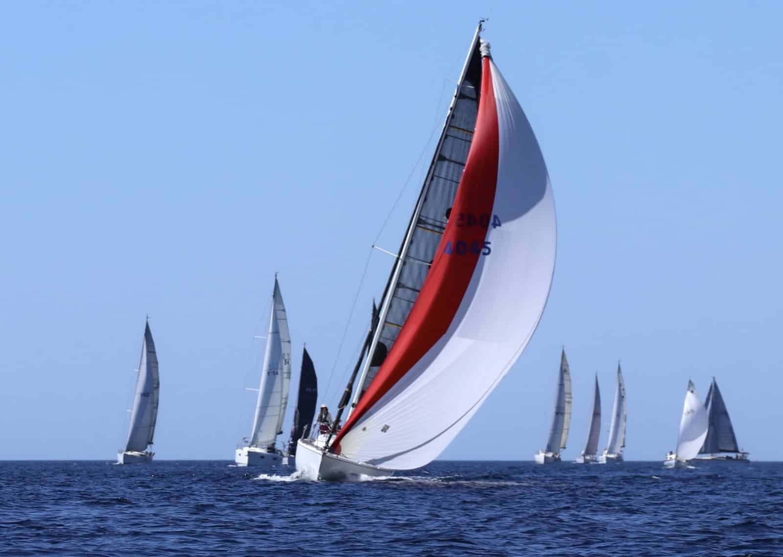 Fleet reaching under spinnakers, lead boat flying a red-and-white kite