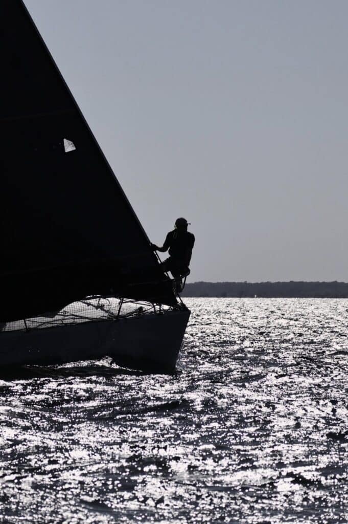 Silhouette of a bow crew member on the bowsprit over glittering water