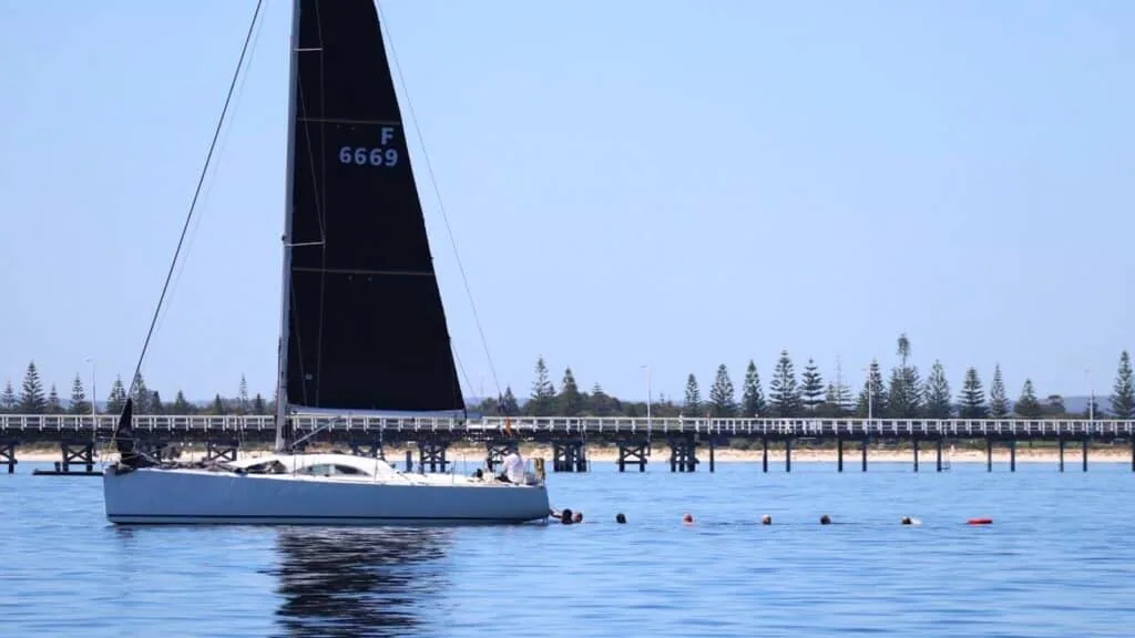 Boat F6669 under a black mainsail gliding past a wooden jetty