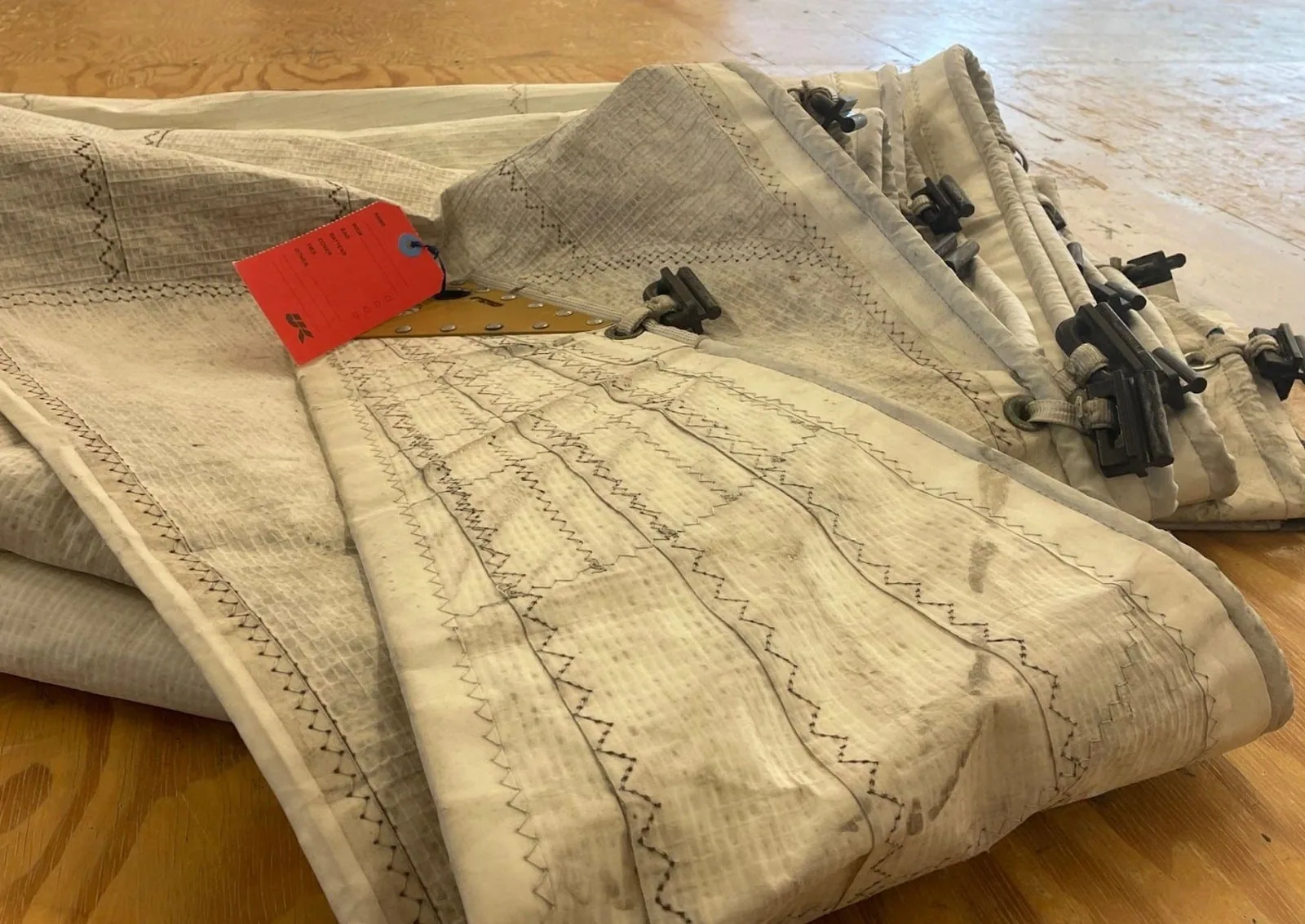 Mildew-stained sail folded on a wood floor with an orange tag