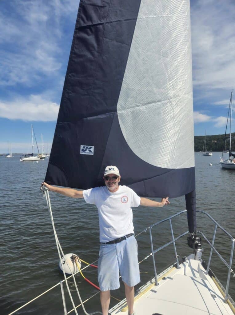 Man beneath a hoisted navy-and-white sail with the UK Sailmakers logo