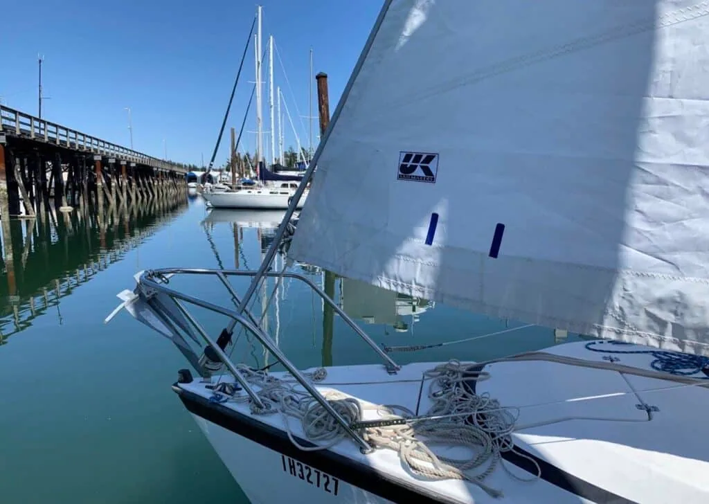 Small dinghy hoisting a UK Sailmakers mainsail beside a dock