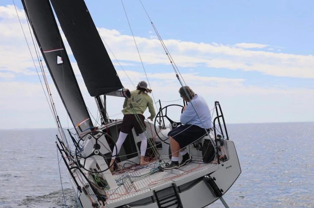 Two crew at the twin wheels of an L30 under black main and jib