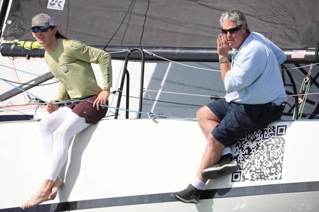 Two sailors on the rail of an L30 hailing a nearby boat