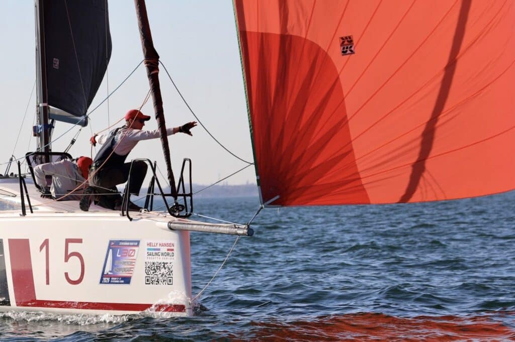 L30 #15 crew trimming a red spinnaker with a printed logo