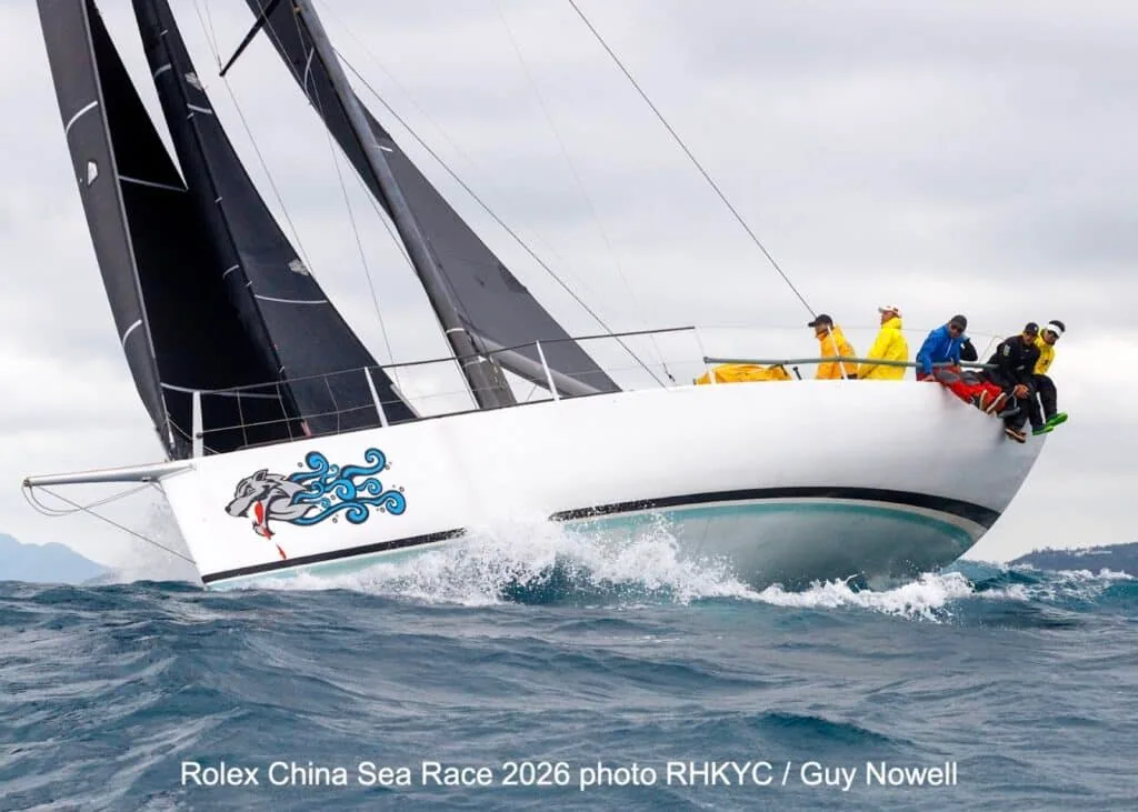 Yacht with dragon-head bow art heeling hard, crew hiked out