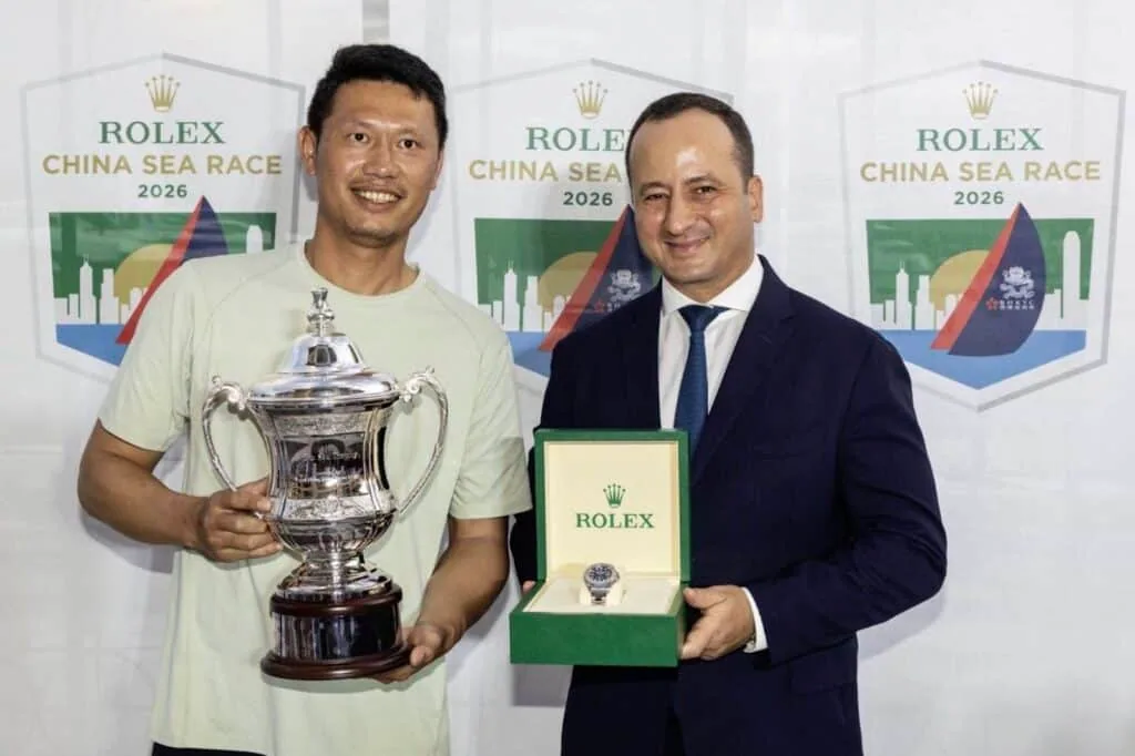 Skipper holding the winner's trophy beside a Rolex representative