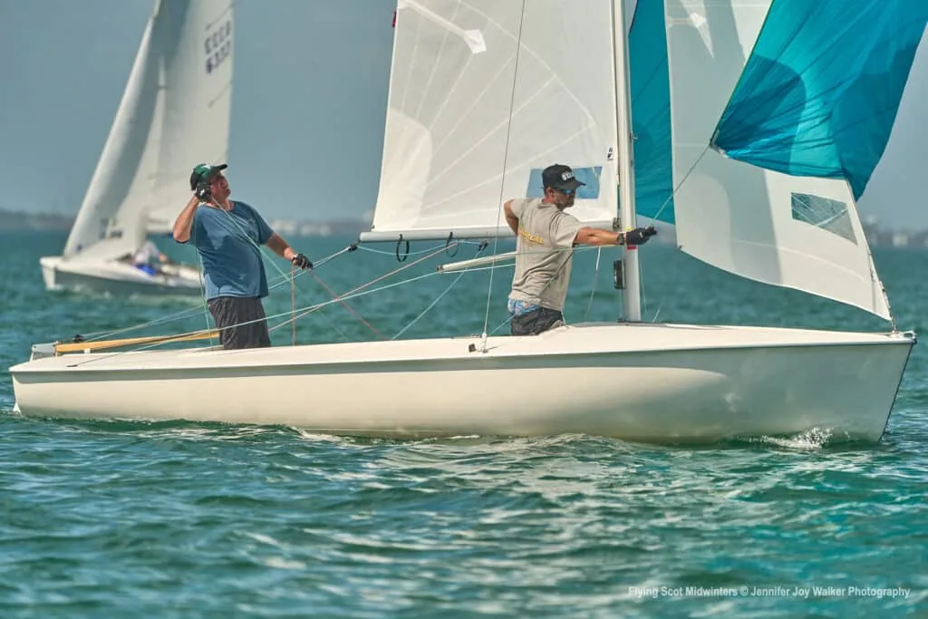 Flying Scot crew hoisting a teal spinnaker before the run