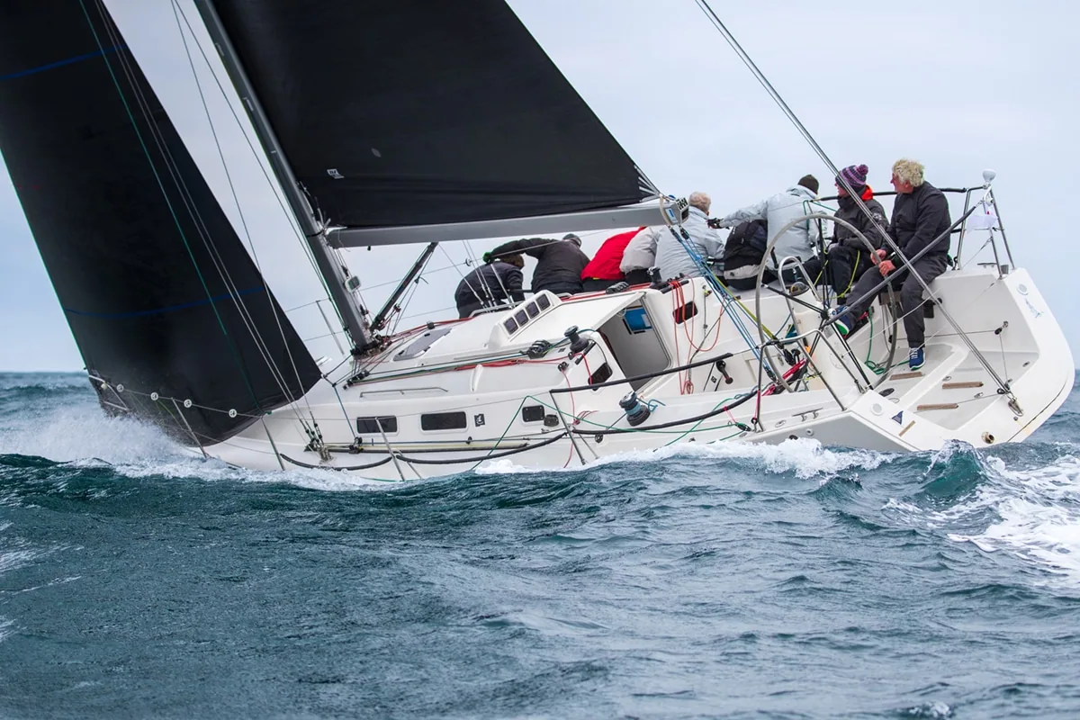 Artful DodJer heeled hard under a black mainsail with crew hiking out