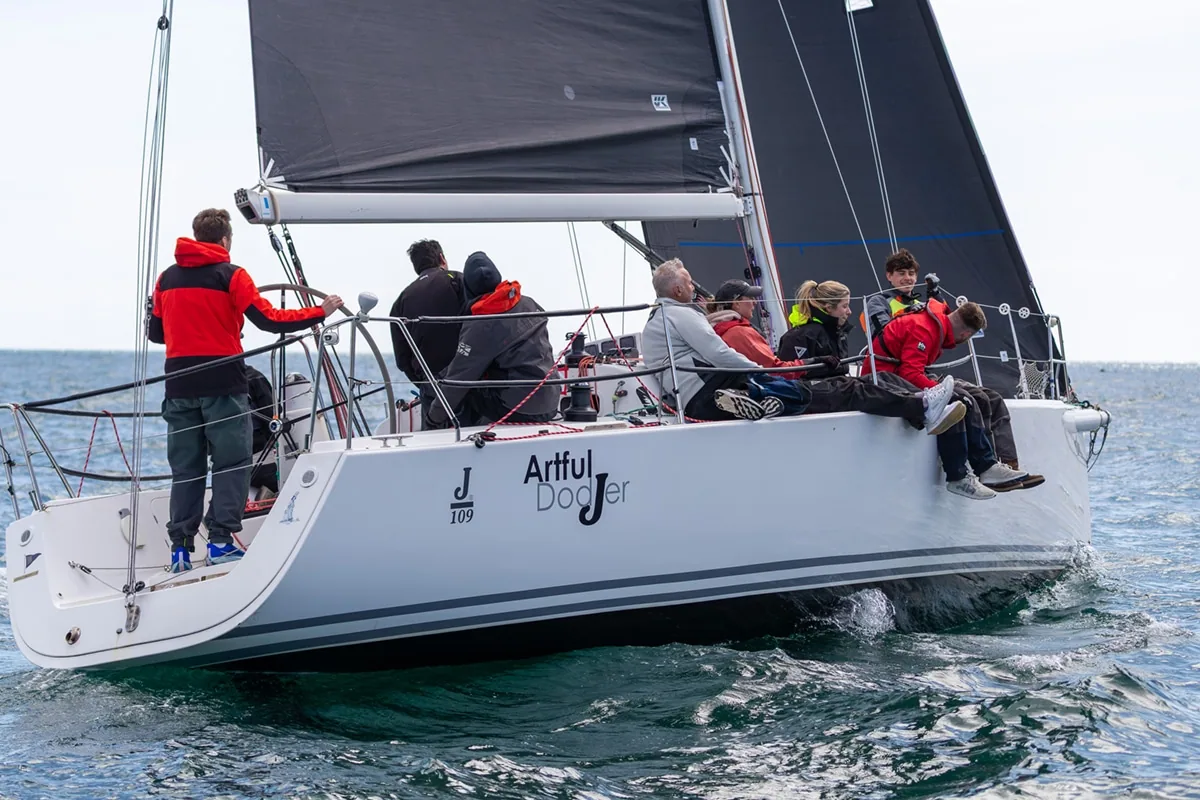 J/109 Artful DodJer's crew hiking out downwind under a black mainsail