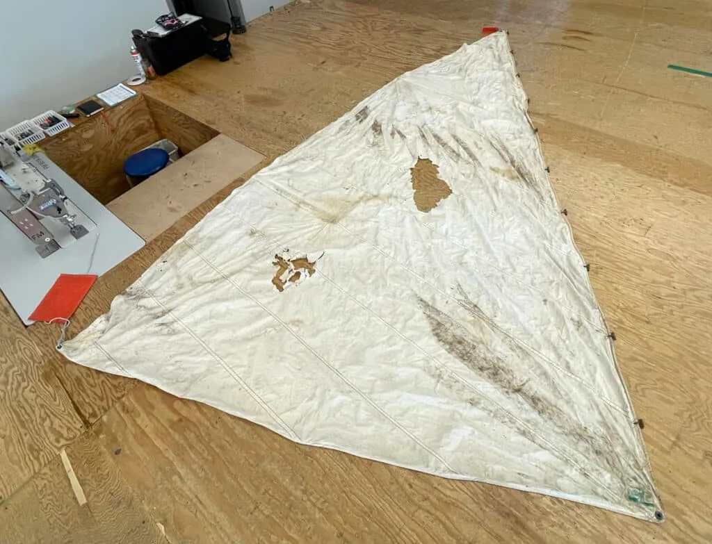 A used sail laid out on the loft floor showing tears and mildew stains