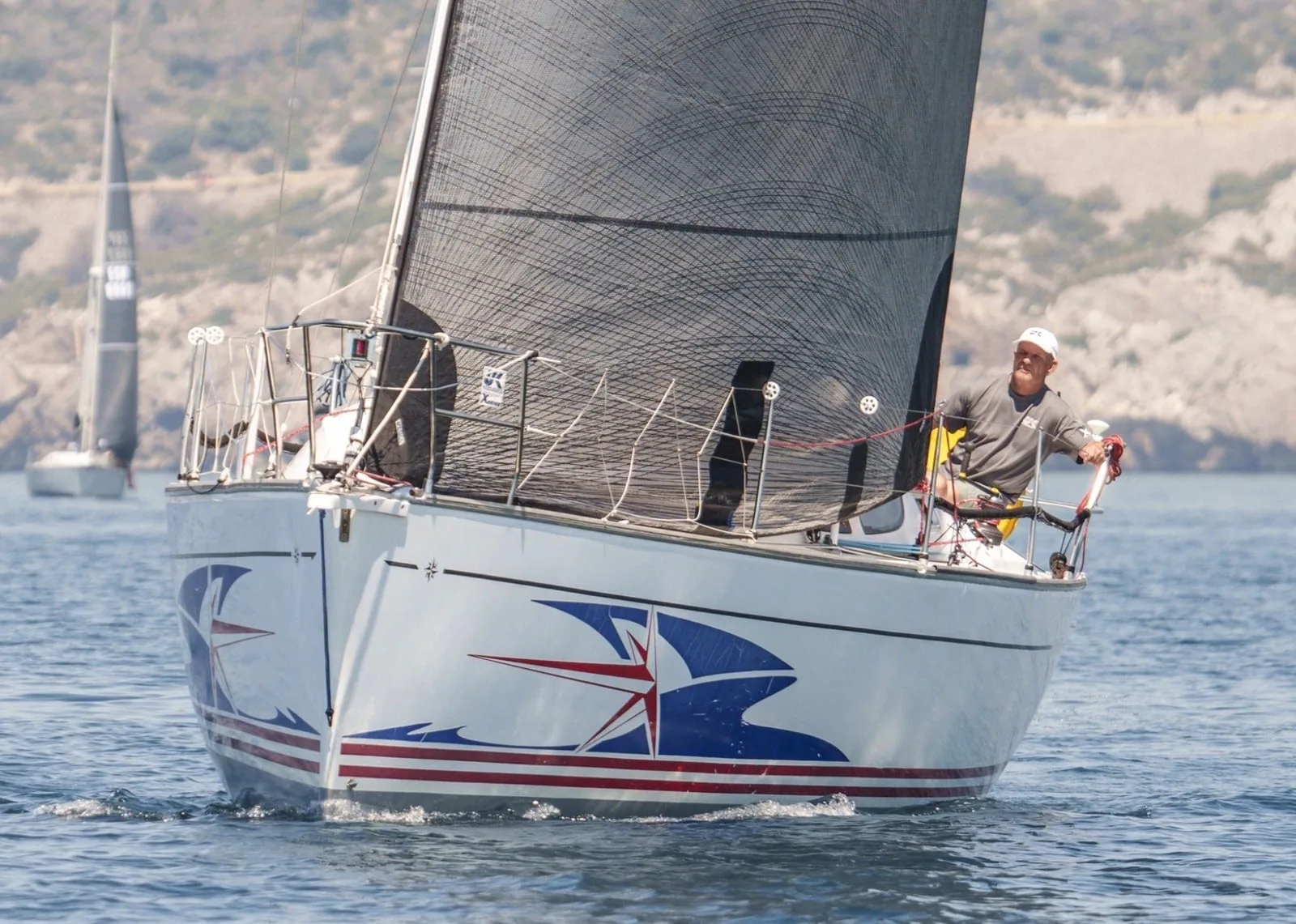 A racer with a red, white and blue star bow graphic sails near a coast