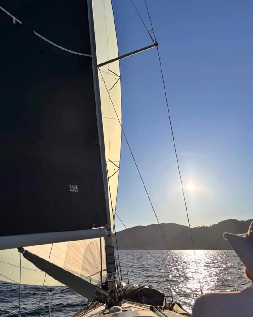 Onboard view of a black mainsail sailing toward hills at golden hour