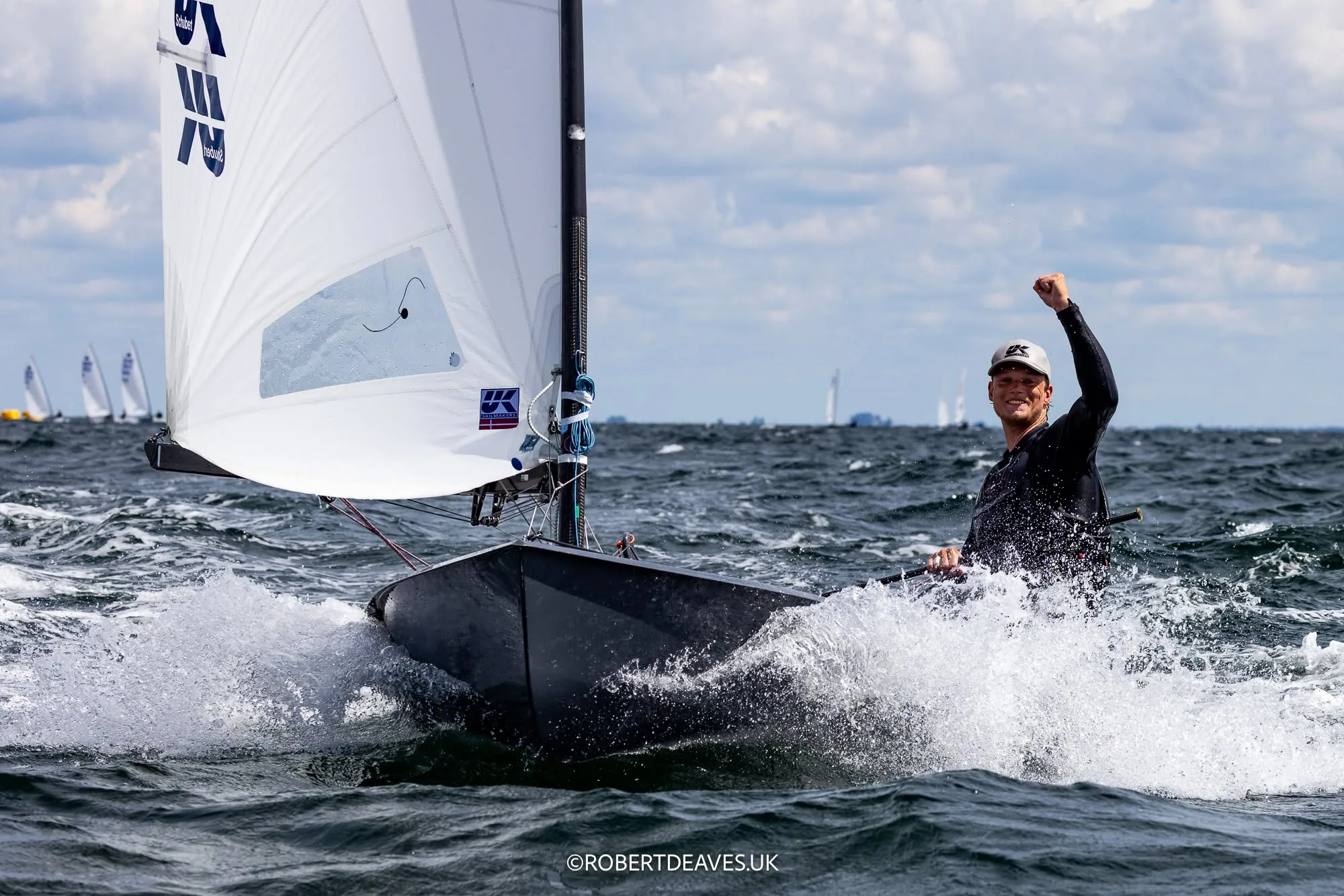 OK Dinghy sailor pumping a fist in celebration, city skyline behind