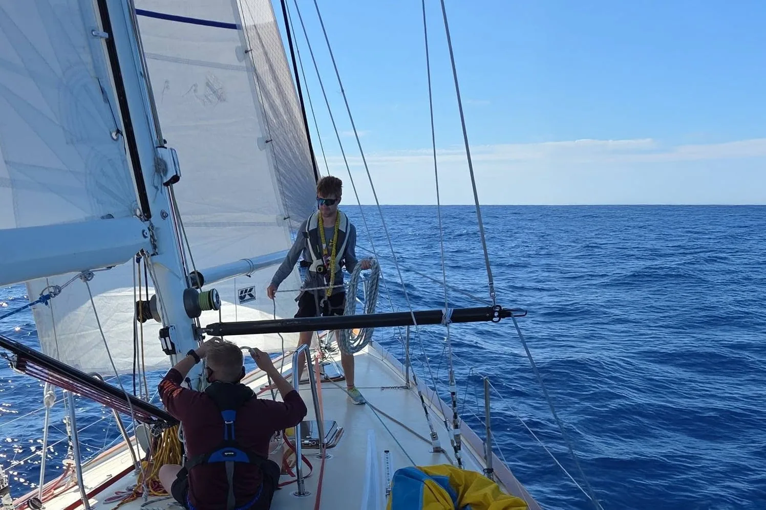 Crew aboard Blue Skies trims sail on open water under a clear sky