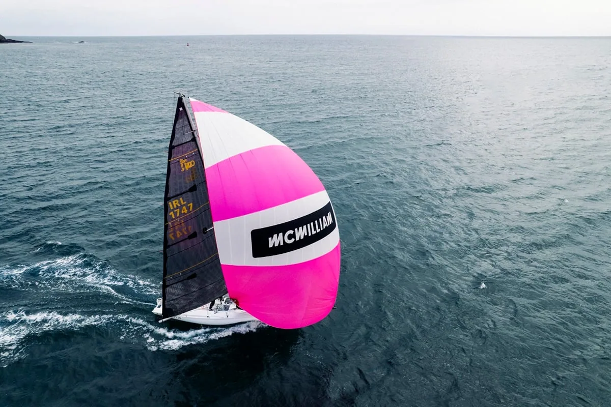 A skiff sails under a pink and white spinnaker branded McWilliam