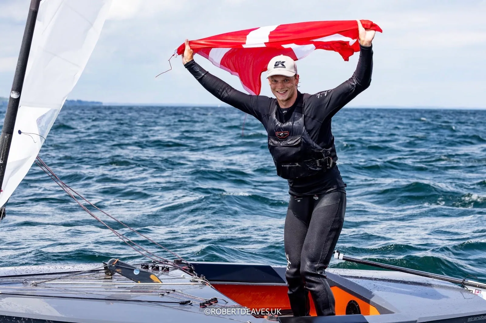 Johan Schubert stands on his OK Dinghy holding a Danish flag after winning Worlds