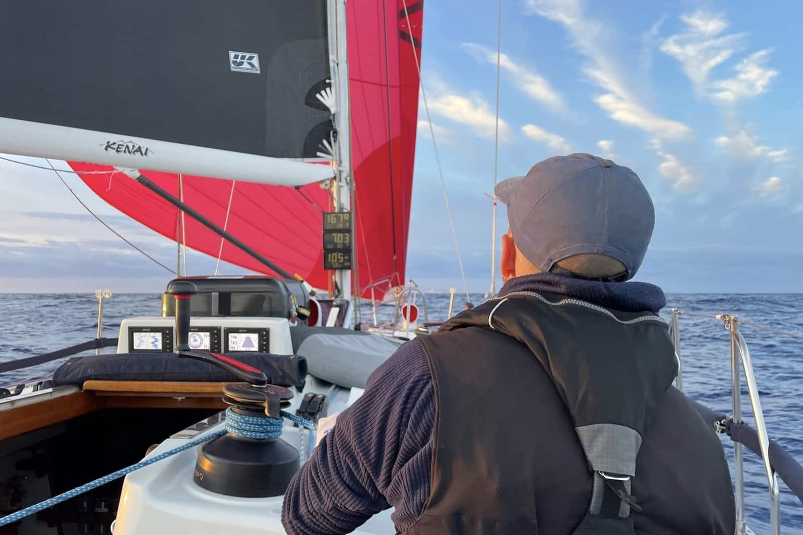 Crew trims Kenai's red gennaker at dusk beside her UK Sailmakers boom cover