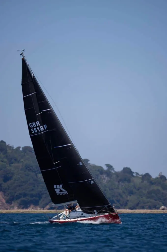 SNAFU sails close-hauled under her black mainsail along the coast