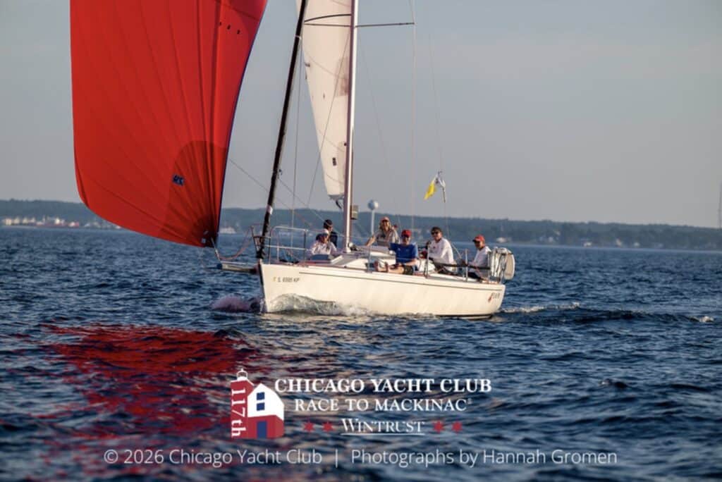 A boat runs downwind under a red spinnaker in calm evening light
