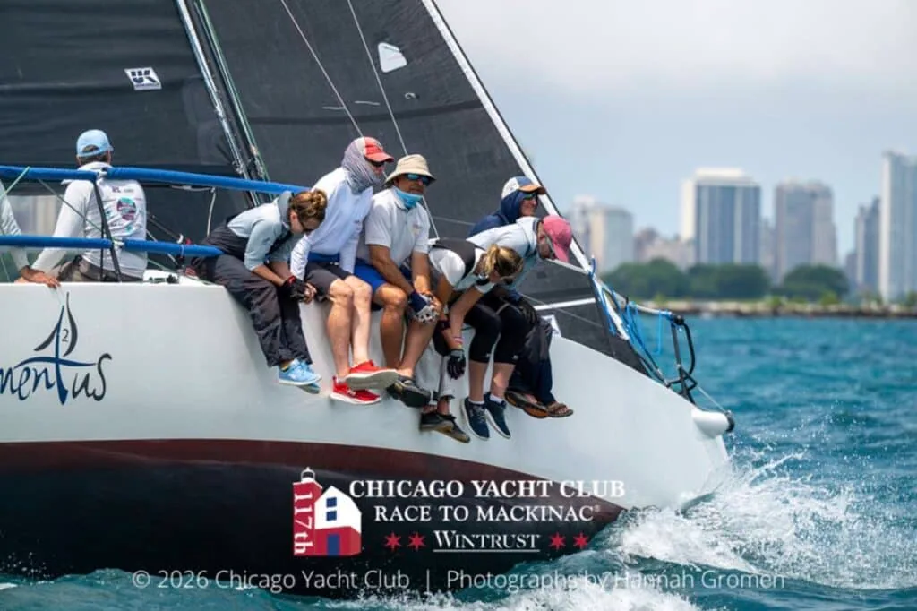 Crew hikes out on a dark-hulled sloop with the Chicago skyline astern