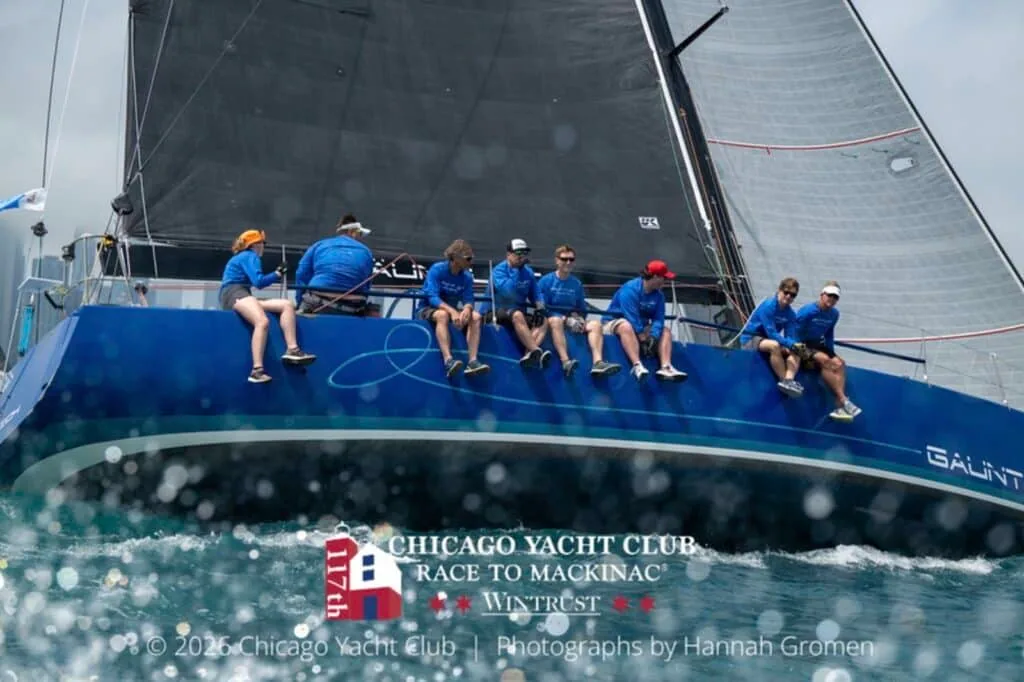 Blue-hulled boat's crew in matching shirts hikes out under a dark mainsail
