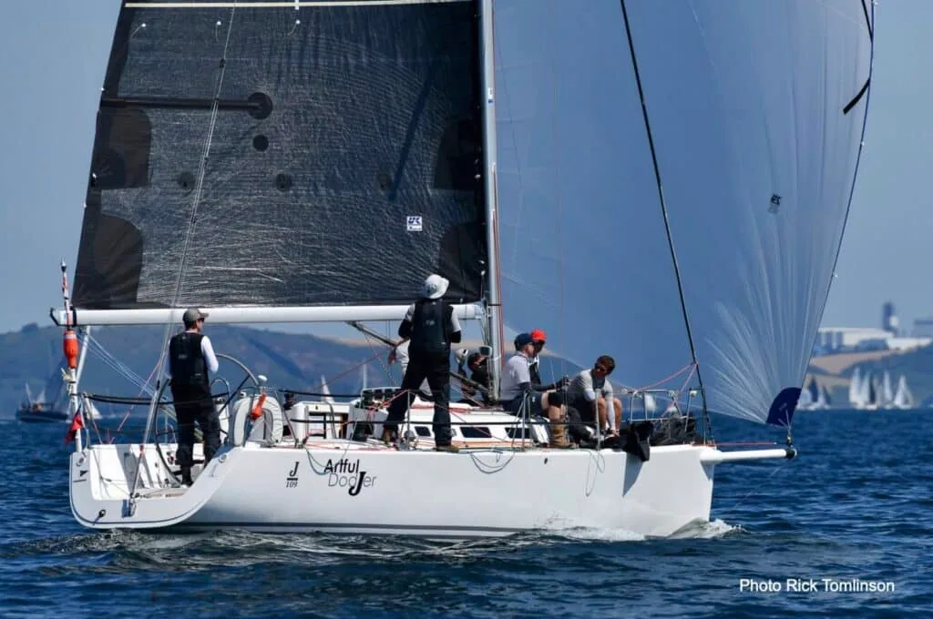 A yacht named Artful flies a blue spinnaker beside her black mainsail