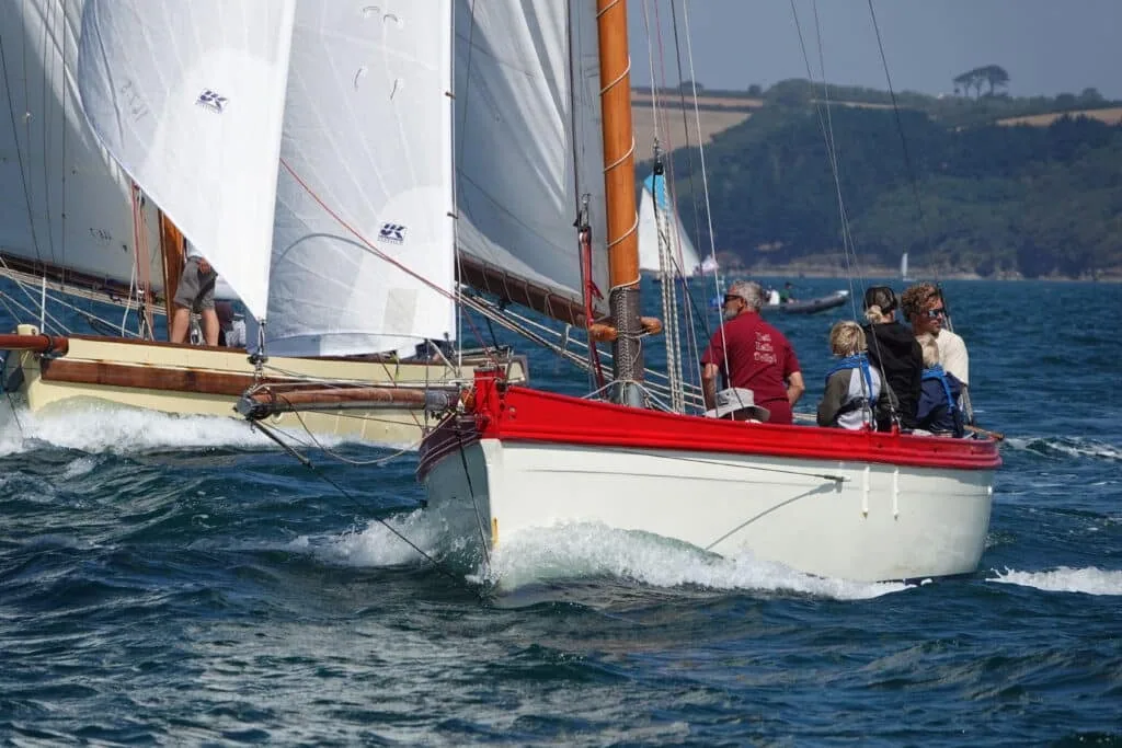 Red-hulled Falmouth Working Boat close-hauled under UK Sailmakers canvas with crew aboard