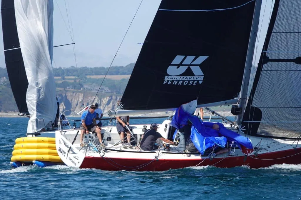 Snafu, a red-hulled racer with black UK Sailmakers Penrose sails, spinnaker being gathered at Falmouth Week