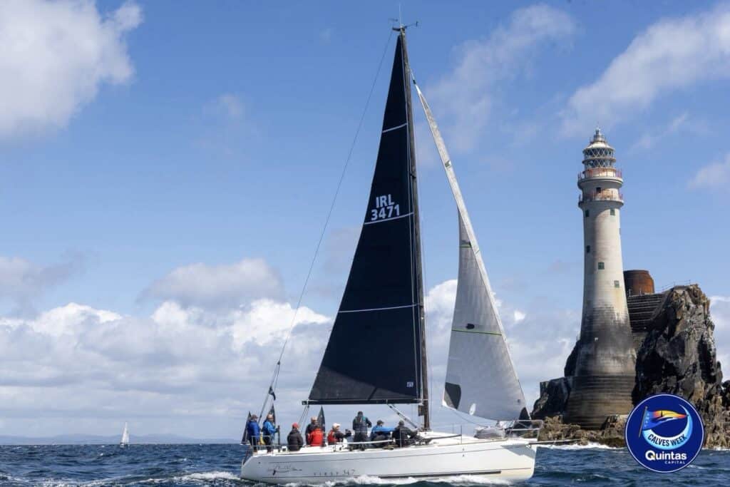 IRL 3471 sails under a dark mainsail past the Fastnet Rock lighthouse