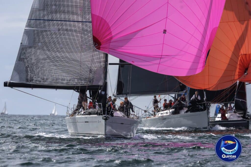 Boats sail close together downwind under pink and orange spinnakers