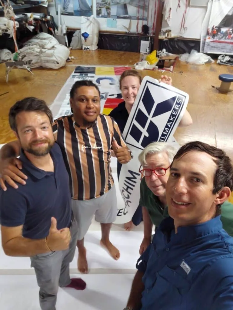 Five people pose at the UK Sailmakers loft with a large custom sail